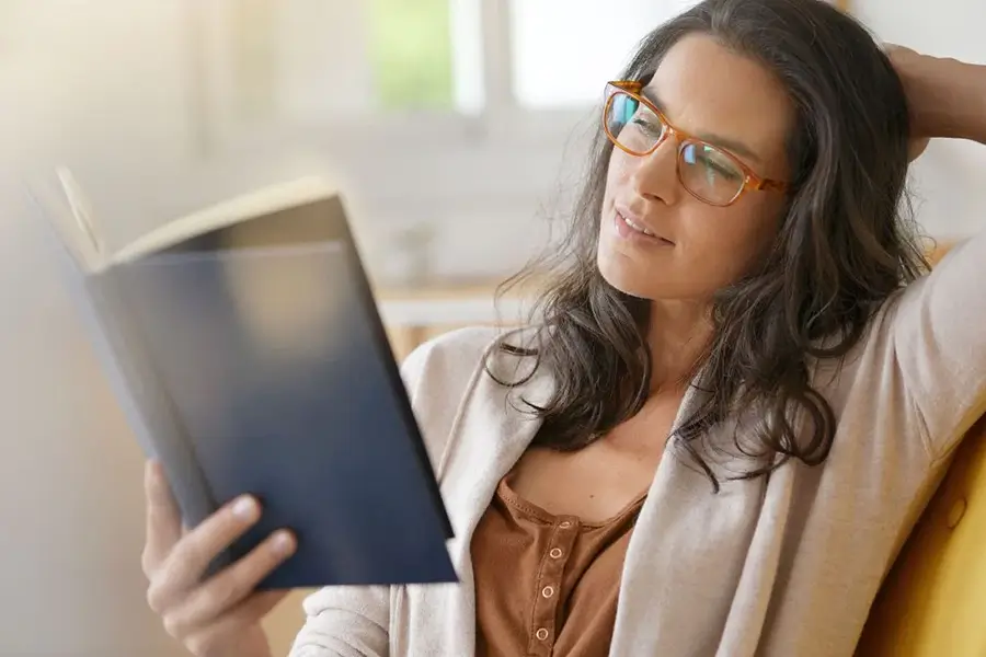 woman using reading glasses to read a book
