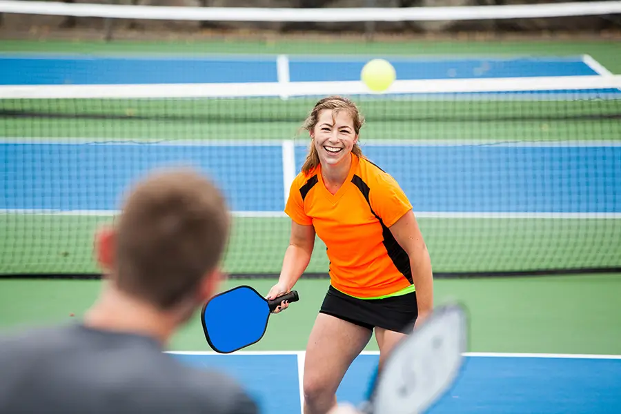 Female pickleball player on court with an orange shirt not using eye protection